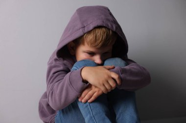 Açık gri duvarın yanında üzgün küçük bir çocuk.