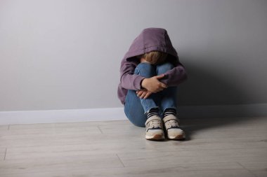 Açık gri duvarın yanındaki üzgün küçük çocuk içeride, mesaj için yer var.