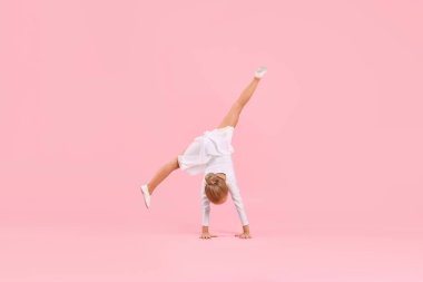 Küçük kız pembe arka plan üzerinde jimnastik yapıyor.