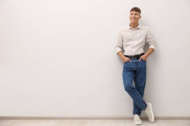 Beyaz duvarın yanında şık kotlu yakışıklı bir genç. Metin için boşluk