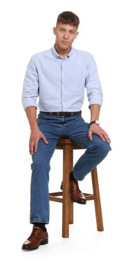 Beyaz arka planda taburede şık kotlar giyen yakışıklı genç adam.