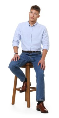 Beyaz arka planda taburede şık kotlar giyen yakışıklı genç adam.