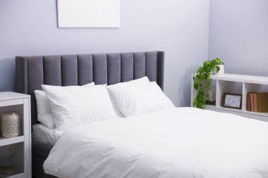 Yatak odasındaki gri duvarın yanında çarşaflı, raflı büyük bir yatak.