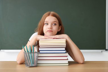 Okula dönelim. Ahşap masada kitap ve kırtasiye malzemesi olan bir öğrenci.