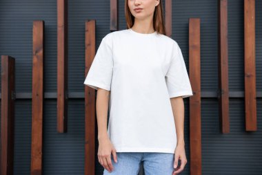 Duvarın yanında beyaz tişört giyen genç bir kadın, yakın plan. Tasarım için model