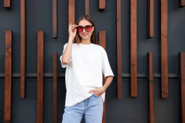 Duvarın yanında beyaz tişört giyen genç bir kadın. Tasarım için model