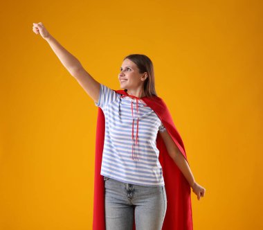 Sarı arka planda süper kahraman pelerini giyen kadın.