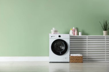 Çamaşır makinesi, deterjanlar ve temiz çamaşır sepeti. Kapalı alandaki yeşil duvarın yanında. Metin için boşluk