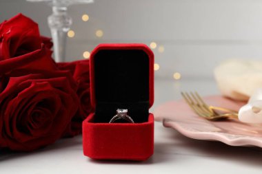 Romantik bir ortam. Nişan yüzüğü, tabak, çatal bıçak takımı ve güller beyaz masada, yakın plan.