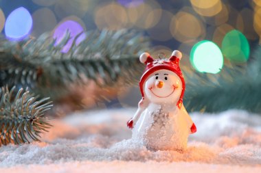 Tatlı dekoratif kardan adam ve köknar ağacı dalları bulanık ışıklara karşı yapay kar üzerinde, yakın plan