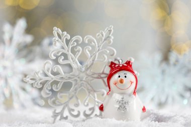 Tatlı dekoratif kardan adam ve kar tanesi suni kar üzerinde bulanık arka plana karşı, yakın plan