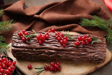 Lezzetli Noel kütüğü (geleneksel Noel pastası) kırmızı üzümlü ve köknar ağacı dallı ahşap masa, yakın plan