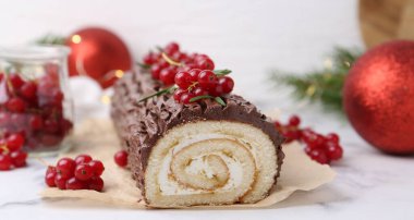 Lezzetli Noel kütüğü (geleneksel Noel pastası) kırmızı frenk üzümü ve dekorlu beyaz masa, yakın plan