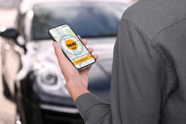 Şehir caddesinde taksi çağırmak için cep telefonu uygulaması kullanan bir adam.