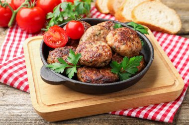 Maydanozlu lezzetli köfteler ve tavada domatesler ahşap masada, yakın plan.