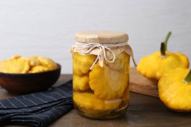 Cam kavanozda turşu kabağı turşusu, kase ve ahşap masa üzerinde açık gri arka plan, yakın plan