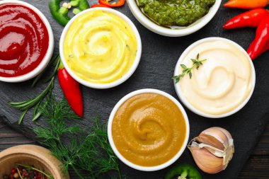 Farklı soslar ve otlar ahşap masada, düz yerde.