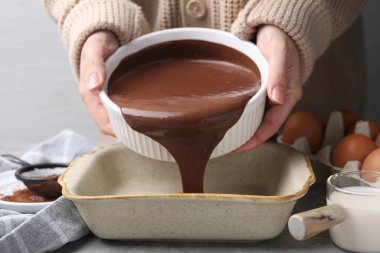 Gri masadaki yemek kabına çikolata hamuru döken kadın, yakın plan.