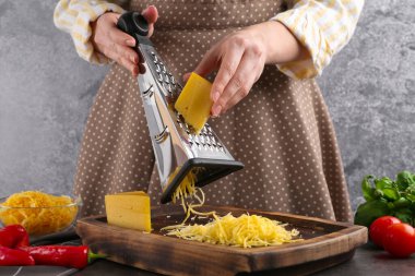 Gri masada peynir rendeleyen kadın, yakın plan.