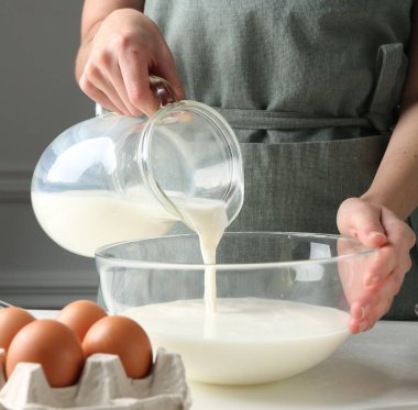 Hamur yapmak (sıvı hamur). Beyaz masadaki kaseye süt döken kadın, yakın plan.