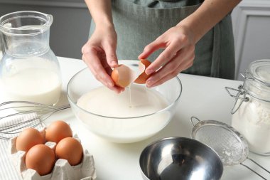 Hamur yapmak (sıvı hamur). Beyaz masadaki kaseye yumurta ekleyen kadın, yakın plan.