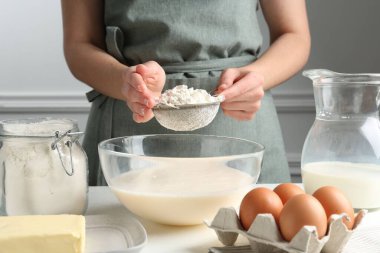 Hamur yapmak (sıvı hamur). Beyaz masada un yiyen bir kadın. Kapalı alanda, yakın plan.