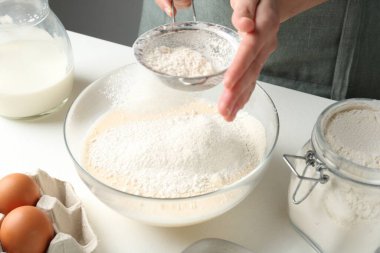 Hamur yapmak (sıvı hamur). Beyaz masada un yiyen bir kadın. Kapalı alanda, yakın plan.