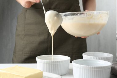 Kadın hamur hamurunu (sıvı hamur) içerideki masada yemek tabaklarına döküyor, yakın plan.