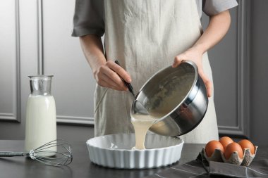 Mutfaktaki gri masada kaseden yemek kabına sıvı hamur döken kadın, yakın plan.