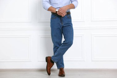 Beyaz duvarın yanında şık kotlu adam, yakın plan.