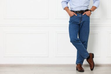 Beyaz duvarın yanında şık kotlu bir adam, yakın plan. Metin için boşluk