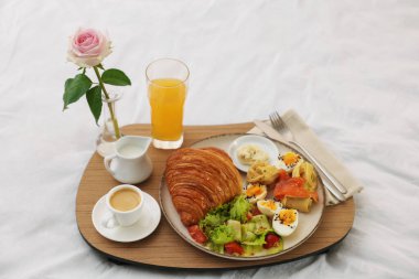 Nefis bir kahvaltı tepsisi ve otel odasında yatakta gül, yakın plan.