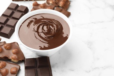 Erimiş çikolata ve parçalarla dolu bir kase beyaz mermer masa, yakın plan. Metin için boşluk