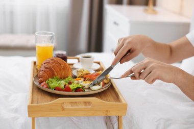 Yatakta nefis bir kahvaltı yapan adam, yakın plan. Otel oda servisi.