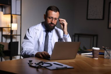 Doktor, gece vardiyası sırasında klinikteki masada dizüstü bilgisayarla çalışıyor.