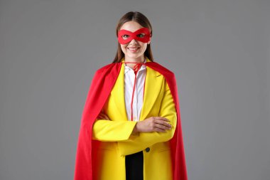 İş kadını gri arka planda süper kahraman kostümü giyiyor.