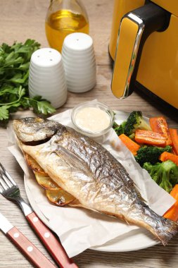 Lezzetli ızgara balık, sebze, sos ve tava ahşap masada, yakın plan.