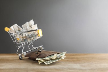 Para biriktiriyorum. Tahta masanın üzerinde dolar banknotları olan mini sepet gri arka planda, mesaj için boşluk