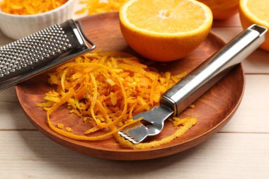 Portakal tadı, taze meyveler, hafif ahşap masada zester aleti ve rende, yakın plan.