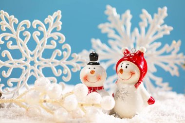 Tatlı dekoratif kardan adam, böğürtlenli dal ve kar taneleriyle yapay kar üzerinde açık mavi arkaplan, yakın plan