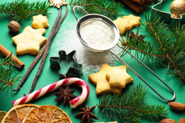 Yıldızlar, kesiciler, köknar ağacı dalları ve yeşil arka planda baharatlar şeklinde kurabiyeler içeren Noel kompozisyonu, yakın plan