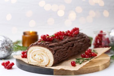 Lezzetli Noel kütüğü (geleneksel Noel pastası) kırmızı üzümlü masada bulanık ışıklara karşı, yakın plan. Bokeh etkisi