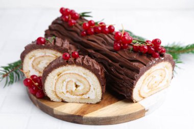 Lezzetli Noel kütüğü (geleneksel Noel pastası) beyaz masa üzerinde kırmızı frenk üzümü, yakın plan