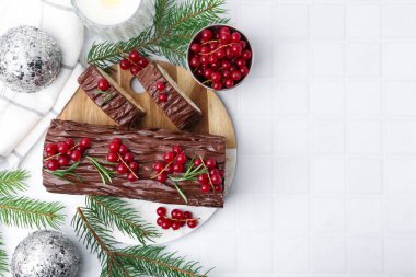 Lezzetli Noel kütüğü (geleneksel Noel pastası) kırmızı frenk üzümü, dekor ve köknar ağacı dallarıyla beyaz döşemeli masa, düz. Metin için boşluk