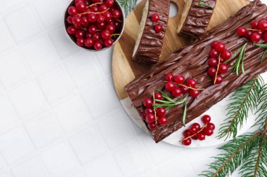 Lezzetli Noel kütüğü (geleneksel Noel pastası) kırmızı frenk üzümü ve köknar dallarıyla beyaz fayanslı masa, düz yatak. Metin için boşluk