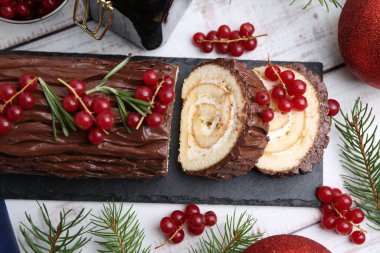 Lezzetli Noel kütüğü (geleneksel Noel pastası) kırmızı frenk üzümü, dekor ve köknar ağacı dalları açık ahşap masa üzerinde, düz yatıyordu