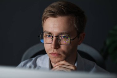 Gri arka planda yansıyan gözlük takan genç bir adam.