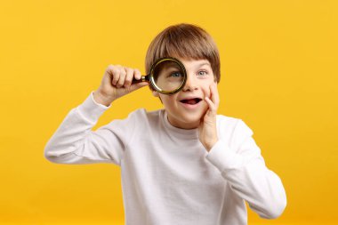 Sarı arka planda büyüteç olan küçük çocuk şaşırdı.