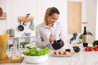 Mutfaktaki masada yemek yapan gülümseyen kadın.