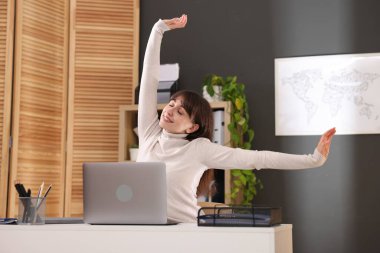 Genç iş kadını kollarını uzatıyor ve ofiste masaya geri dönüyor.